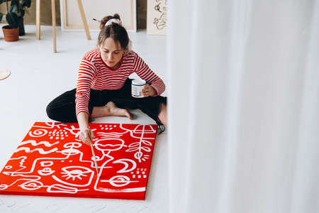 Young woman painting on canvas while sitting on floorの写真素材
