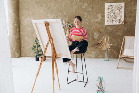 Woman with paintbrush and color palette sitting at studioの写真素材
