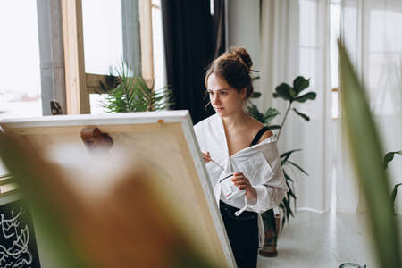 Female painter standing near easel and drawing with brushの写真素材