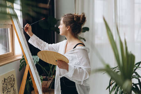 Side view of young woman painting on canvas with brushの写真素材