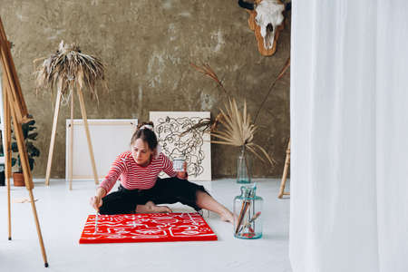 Attractive woman sitting on floor and painting on red canvasの写真素材