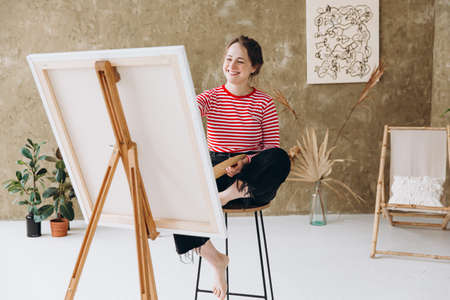 Cheerful female artist painting on easel at studioの写真素材