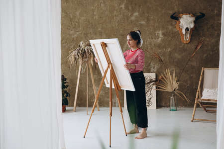 Woman standing in front of easel and painting with brushの写真素材