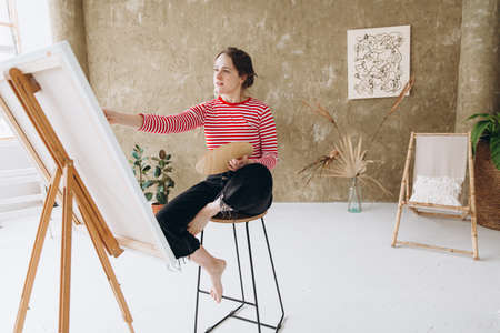 Inspired woman painting on easel with brushの写真素材