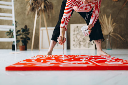 Female artist in earphones painting on red canvas