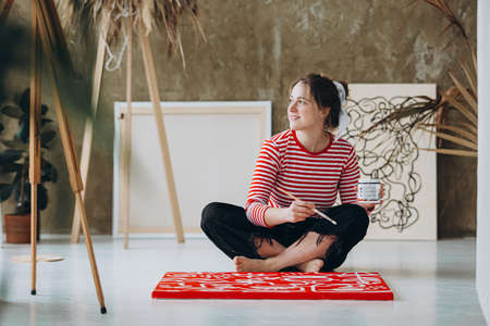 Woman sitting on floor near red canvas and looking asideの写真素材