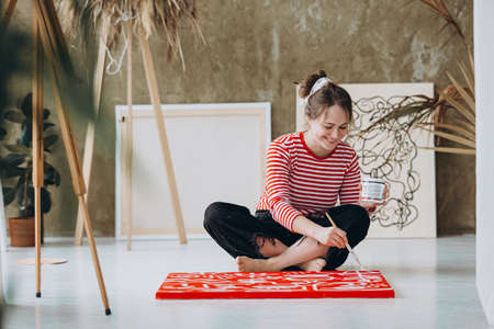 Smiling female artist painting with brush on canvasの写真素材