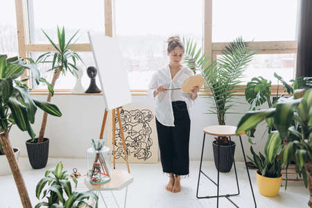Adorable woman mixing paints on wooden palette with brushの写真素材