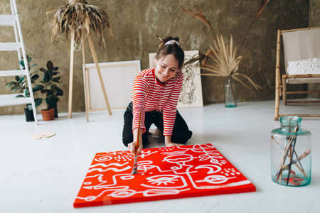 Happy woman painting on red canvas with white colorの写真素材