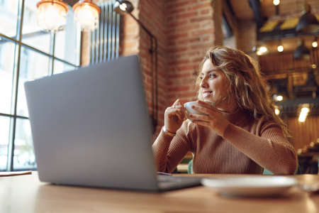 Woman drinking coffee and working on laptop at cafeの写真素材
