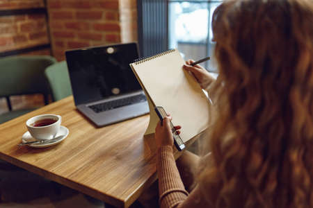 Woman using smartphone and writing in notebookの写真素材