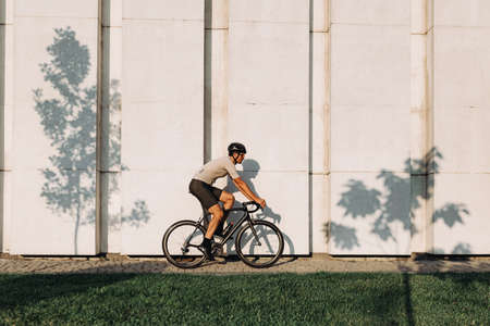 Smiling caucasian man in sport clothes, helmet and glasses practicing in cycling at urban area. Concept of healthy lifestyles and active hobby.の写真素材
