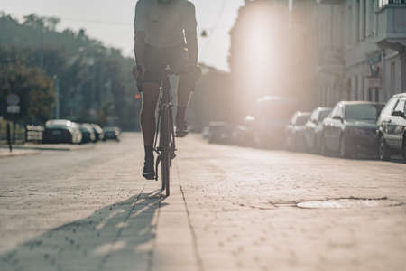 Caucasian cyclist in sportswear looking on mobile screen while standing on city street with black bike. Man taking break during workout outdoors.の写真素材