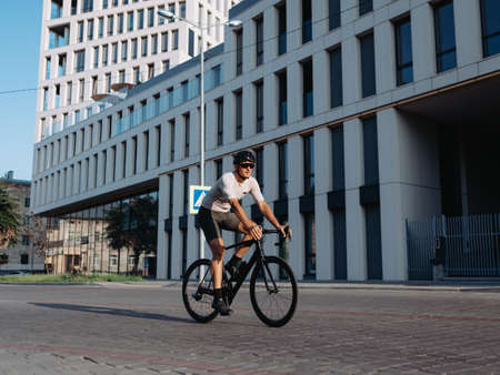 Caucasian cyclist in sportswear looking on mobile screen while standing on city street with black bike. Man taking break during workout outdoors.の写真素材