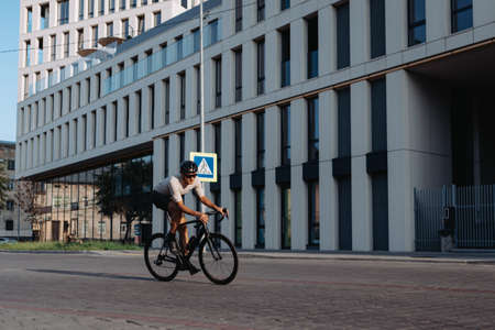 Male athlete in sport clothes and helmet posing with his professional bike on streets of old city. Caucasian man resting during active morning workout.の写真素材