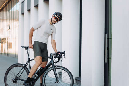 Side view of caucasian man in safety helmet and mirrored glasses riding black bike on city streets. Active cyclist training regularly on fresh air during leisure time.の写真素材