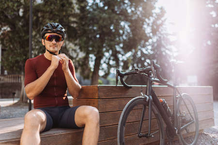 Caucasian male athlete taking break outdoors during morning cyclist. Positive young man sitting on bike and looking aside. Favorite sport hobby.の写真素材