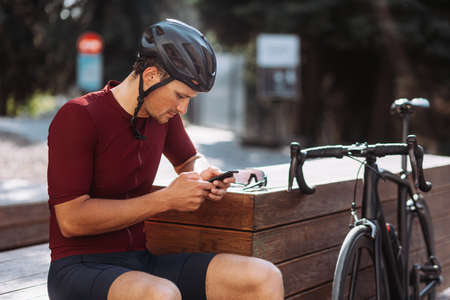 Caucasian male athlete taking break outdoors during morning cyclist. Positive young man sitting on bike and looking aside. Favorite sport hobby.の写真素材