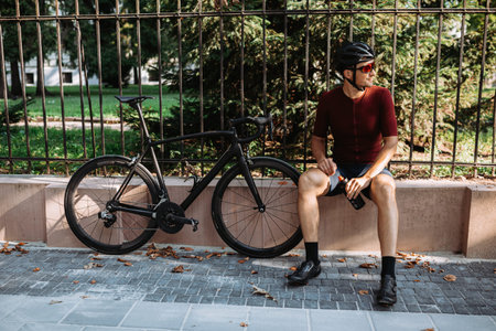 Caucasian male athlete taking break outdoors during morning cyclist. Positive young man sitting on...
