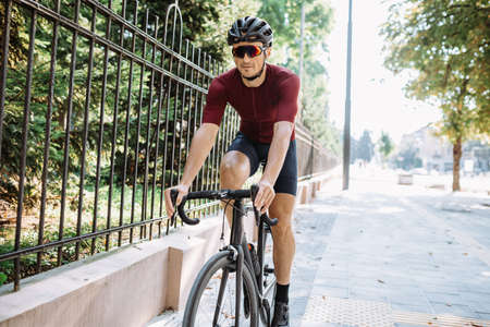 Sporty young man in helmet and glasses spending morning time for outdoors training on black sport bike. Professional cyclist spending every free moment for workout.の写真素材