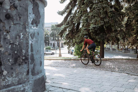 Muscular caucasian man in safety helmet and mirrored glasses using black bike for outdoors training. Cyclist spending morning time for intense workout on city street.の写真素材