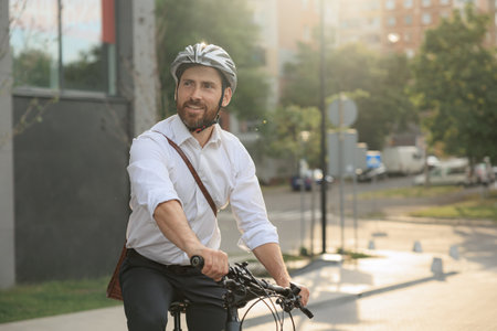 Happy bearded employee on bicycle, going down street in the morning. Front view of elegant man in white shirt smiling, driving bike, while commuting in urban area, with copy space. concept of lifestyle.の写真素材