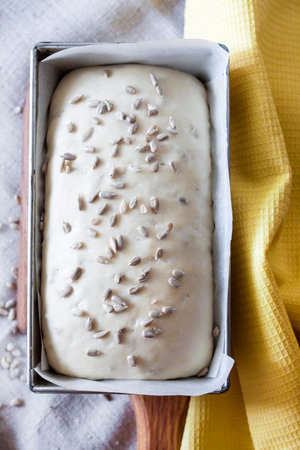 Raw yeast dough in square tin form, ready for baking bread with sunflower seeds