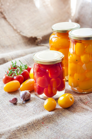 Glass jars with homemade red and yellow pickled tomatoes, sealed with metal lidの写真素材