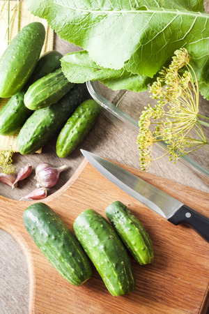 Fresh cucumbers on wooden board prepared for pickling in glass containerの写真素材