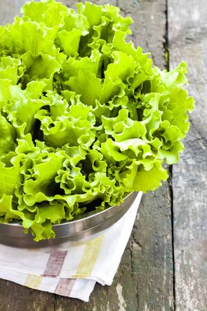 Fresh lettuce leaves in metal bowl on old wooden table in the gardenの写真素材
