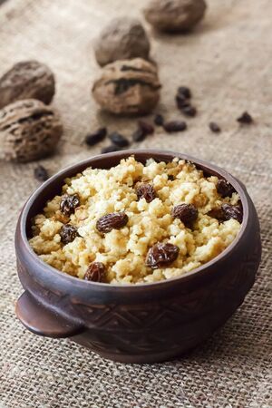 Sweet millet porridge with dark raisins in ceramic rustic bowl with walnuts on backgroundの写真素材