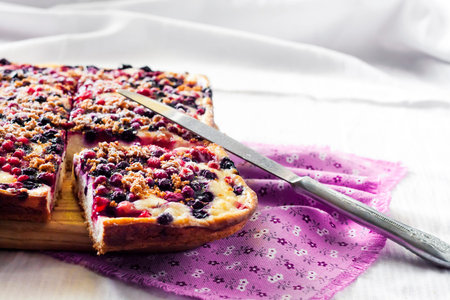 Delicious pie with berry assortment and cottage cheese cut on square slices on a wooden board