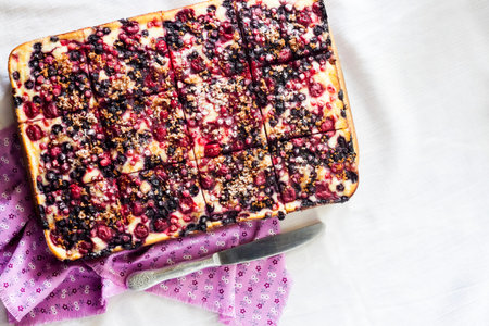 Delicious pie with berry assortment and cottage cheese cut on square slices on a wooden board. Flat...