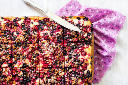 Delicious pie with berry assortment and cottage cheese cut on square slices on a wooden board. Flat...