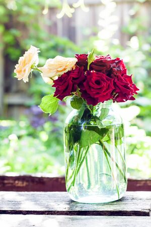 Vintage rose bouquet in glass jar on blurred green garden background in sunny summer dayの写真素材