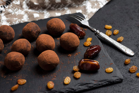 Homemade vegan truffles with dried fruits, walnuts and raw cocoa powder served on black slate plate.