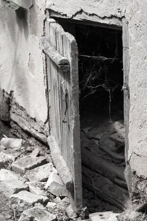 Slightly opened old weathered wooden door and spider web on a darkness background. Scaring backgroundの写真素材