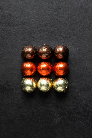 Chocolate candies wrapped in multicolored foil placed on black background in a shape of square, with...