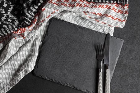 Black slate plate with fork and knife on black background and tablecloth. Table setting.の写真素材