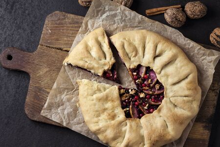Homemade galette pie with apples, elder berries and walnuts decorated with fresh cowberry on rustic dark backgroundの写真素材