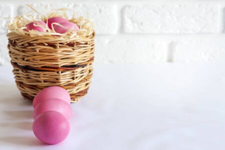 Minimalistic Easter composition with wicker basket and pink colored eggs on white background. Copy spaceの写真素材