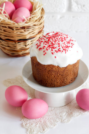 Minimalistic Easter composition with wicker basket with pink colored eggs and Easter cake on white...