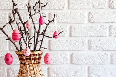 Easter composition with tree branches in a wicker vase decorated with pink colored eggs on white...