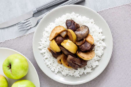 Fried chicken liver with apples served with white rice on a plate. Green apples on background. Flat lay, top viewの写真素材