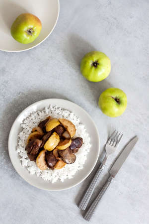 Fried chicken liver with apples served with white rice on a plate. Green apples on background. Flat lay, top viewの写真素材