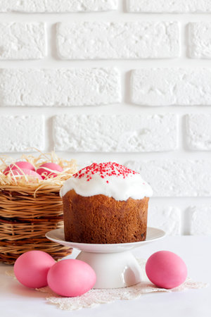 Minimalistic Easter composition with wicker basket with pink colored eggs and Easter cake on white...