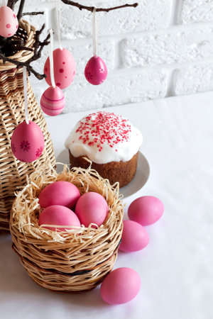 Easter composition with decorated tree branches in a wicker vase, pink colored eggs in wicker basket...