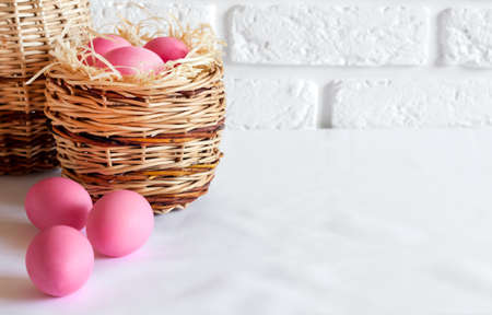 Minimalistic Easter composition with wicker basket and pink colored eggs on white background. Copy spaceの写真素材