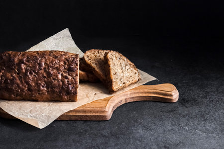 Bread with sunflower and flax seeds on a wooden cutting board on a black background