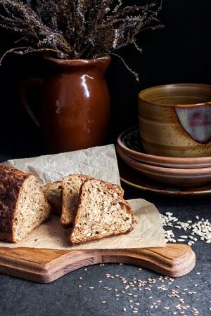 Bread with sunflower and flax seeds on a wooden cutting board. Ceramic crockery in the background.